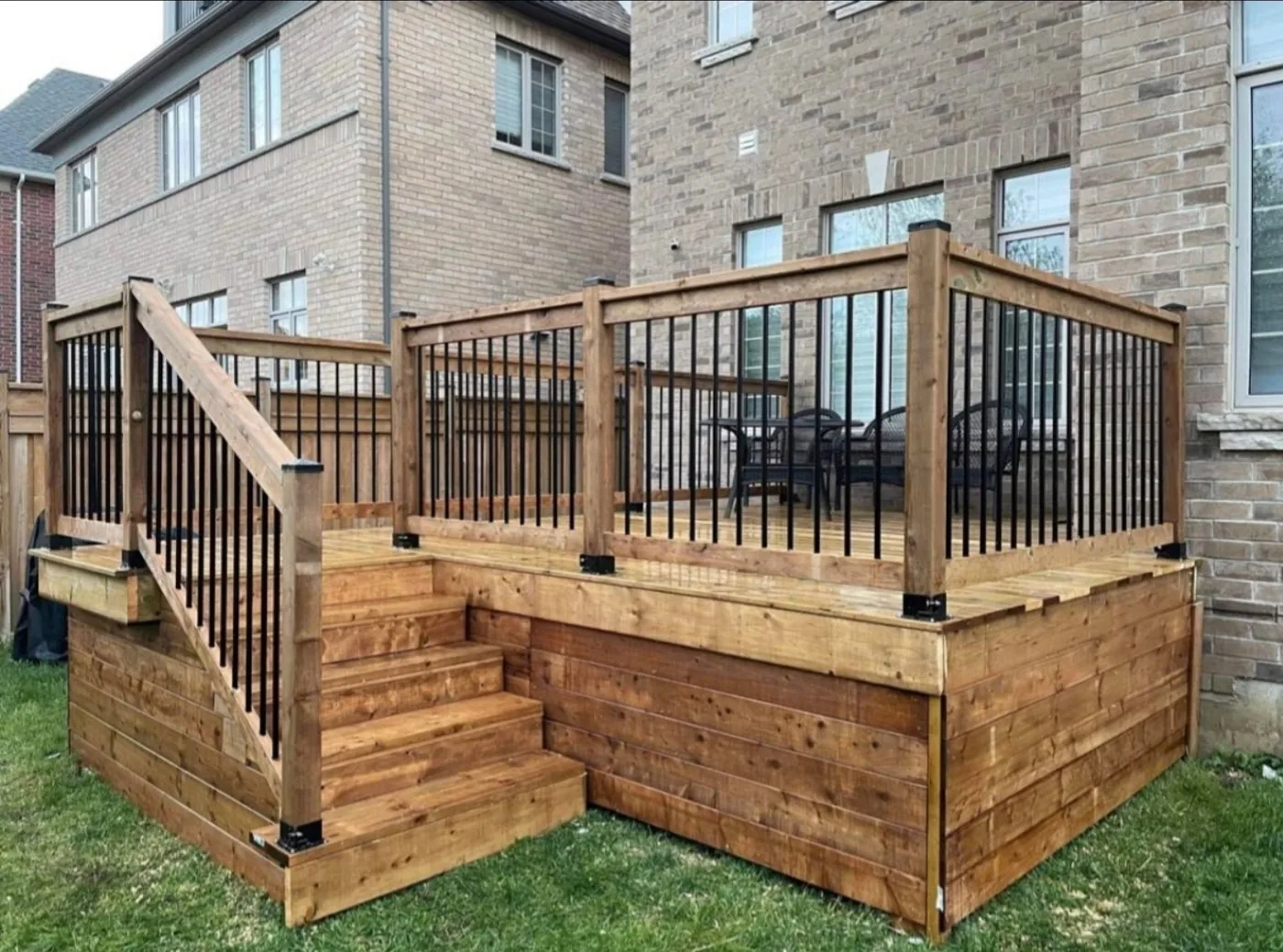 Raised pressure-treated deck with black aluminum railings and wide steps to the lawn, Caledon