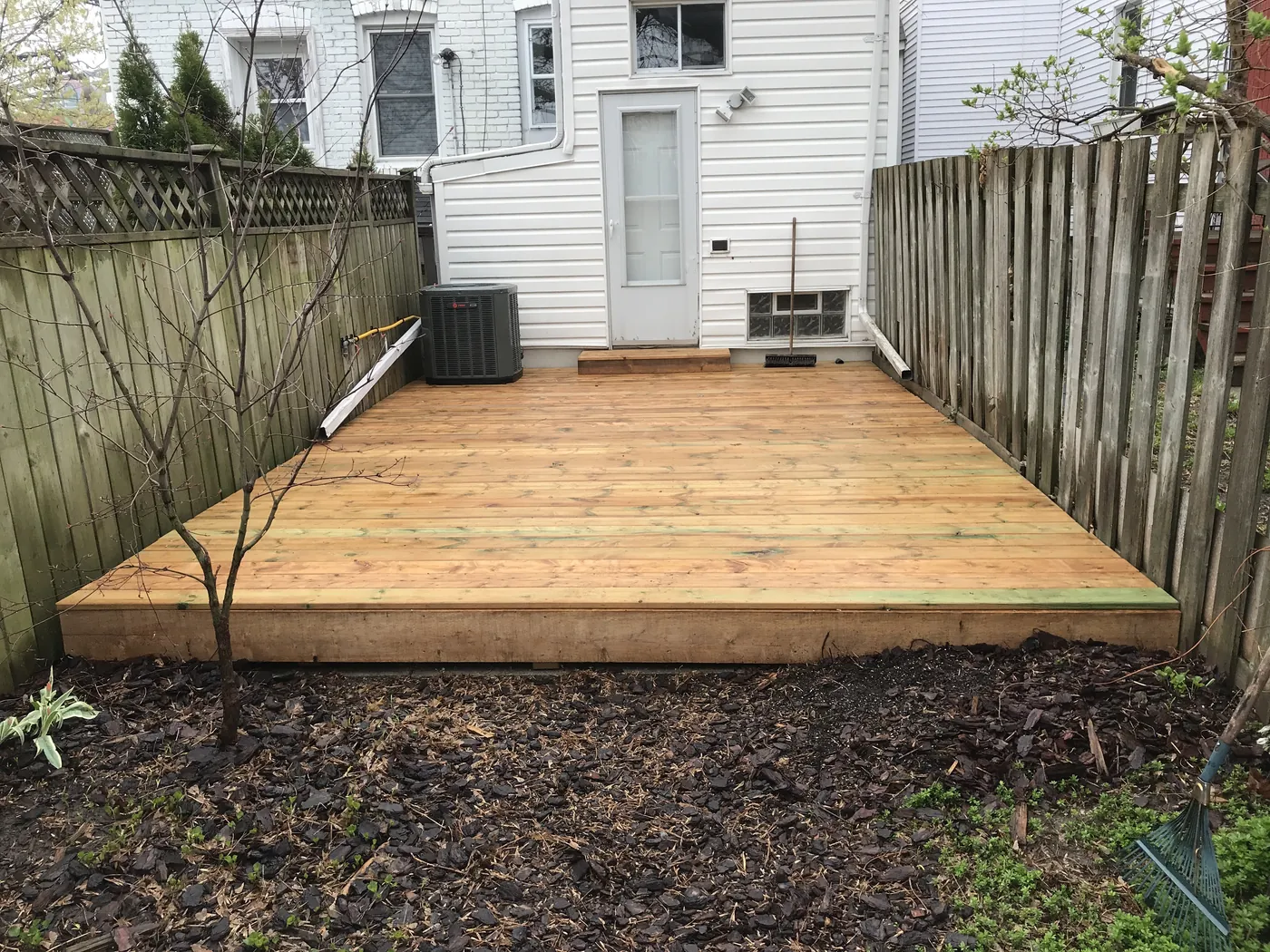 Ground-level pressure-treated deck filling the width of a narrow city garden, East York