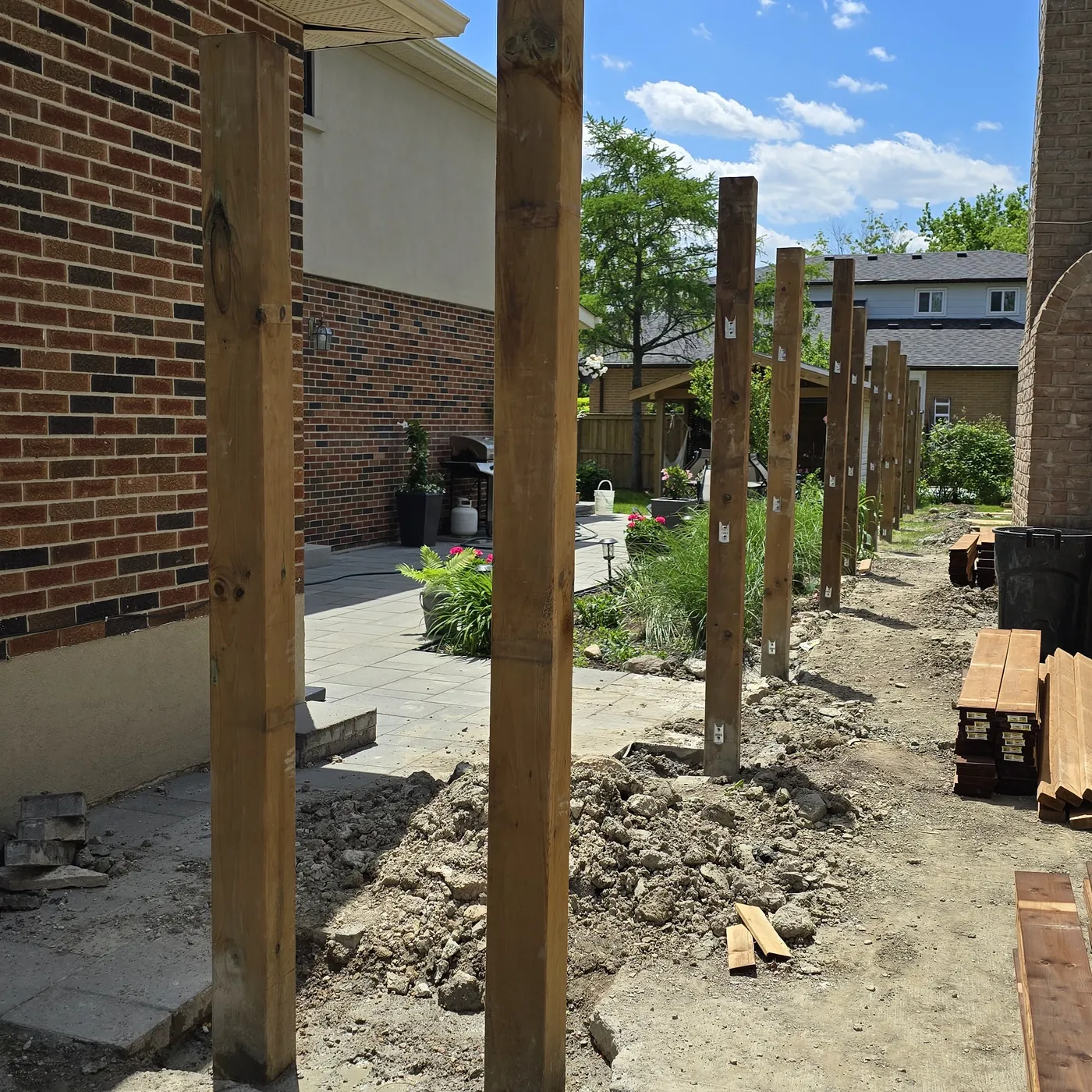 New pressure-treated fence posts standing in line along the side of the house, Markham