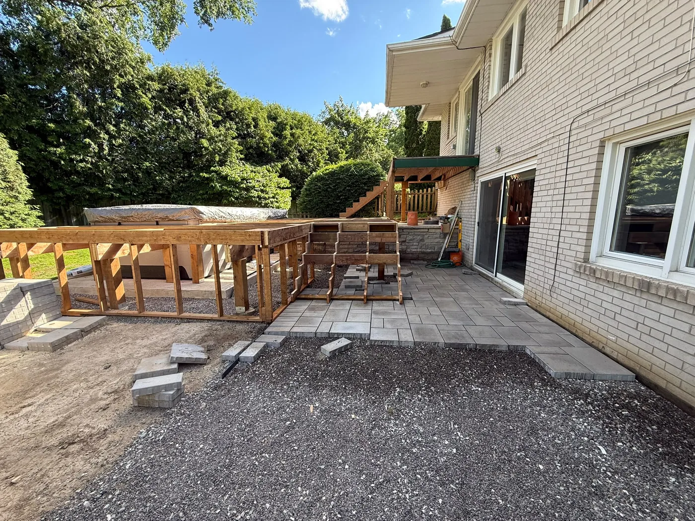 Stone paver patio laid and the deck structure going up beside it in North York