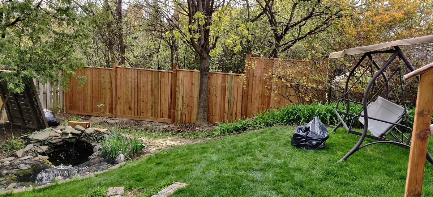 Pressure-treated privacy fence running past mature trees along an Oakville property line
