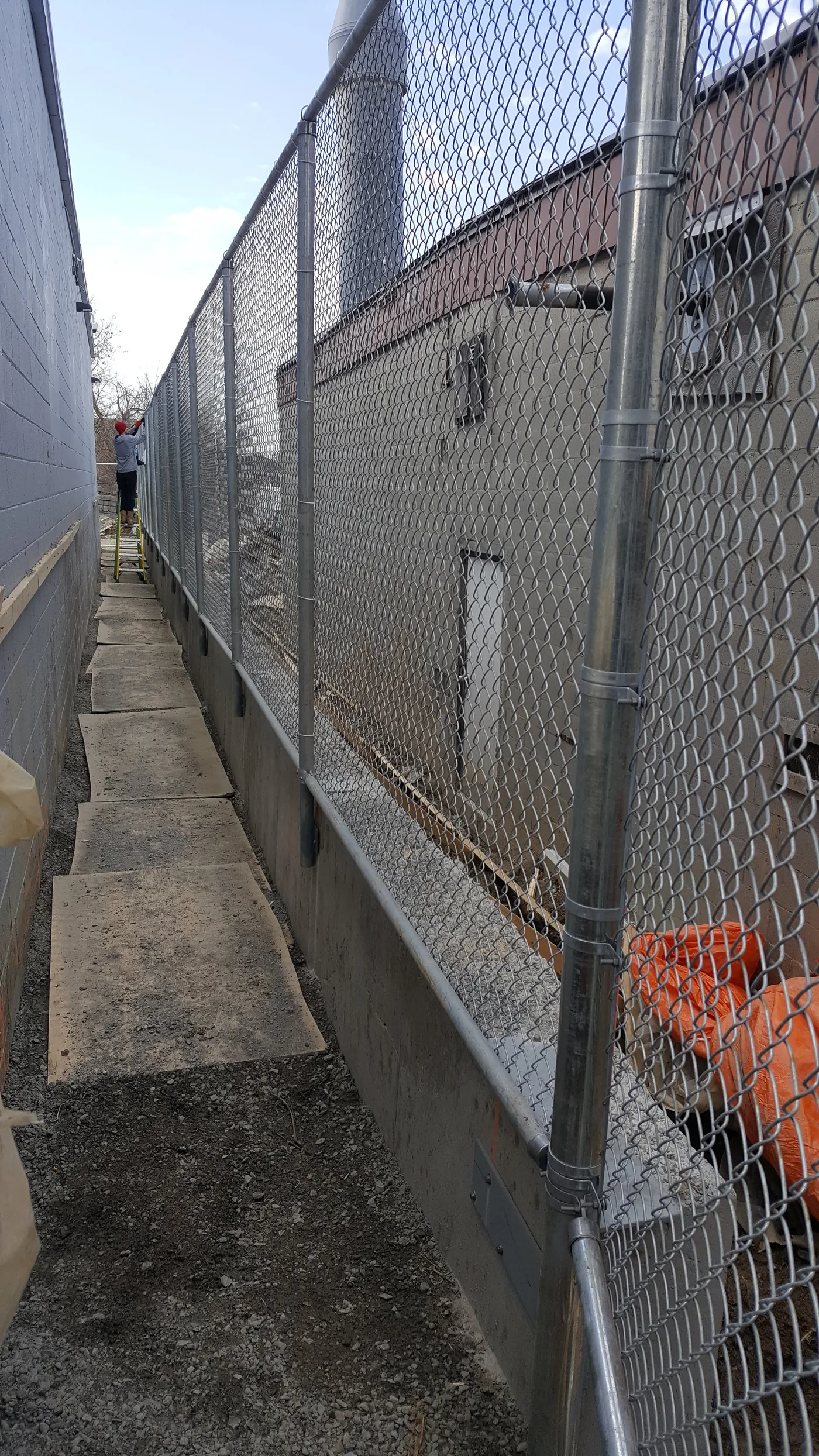 Galvanized chain link carried on a concrete knee wall between two industrial buildings, Scarborough