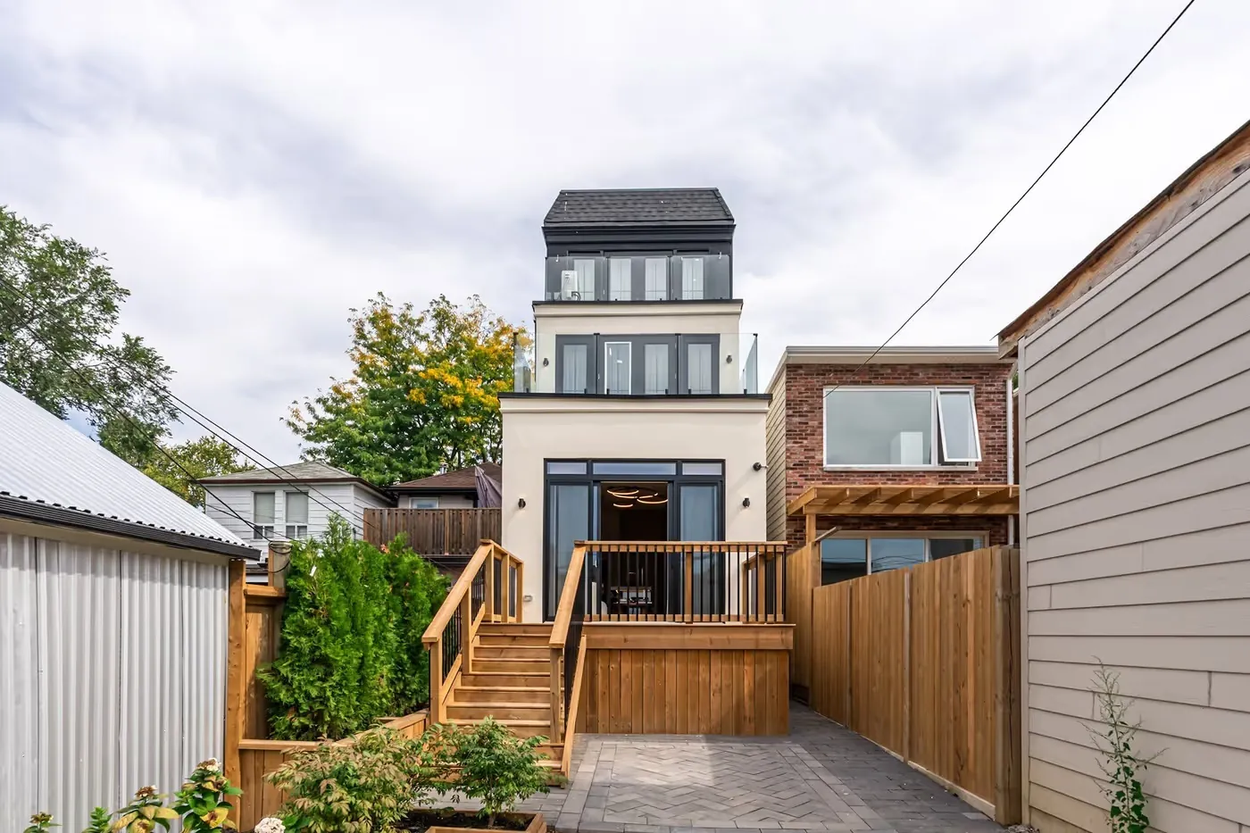 Raised rear deck with black railings above a paved patio and cedar fence, Toronto