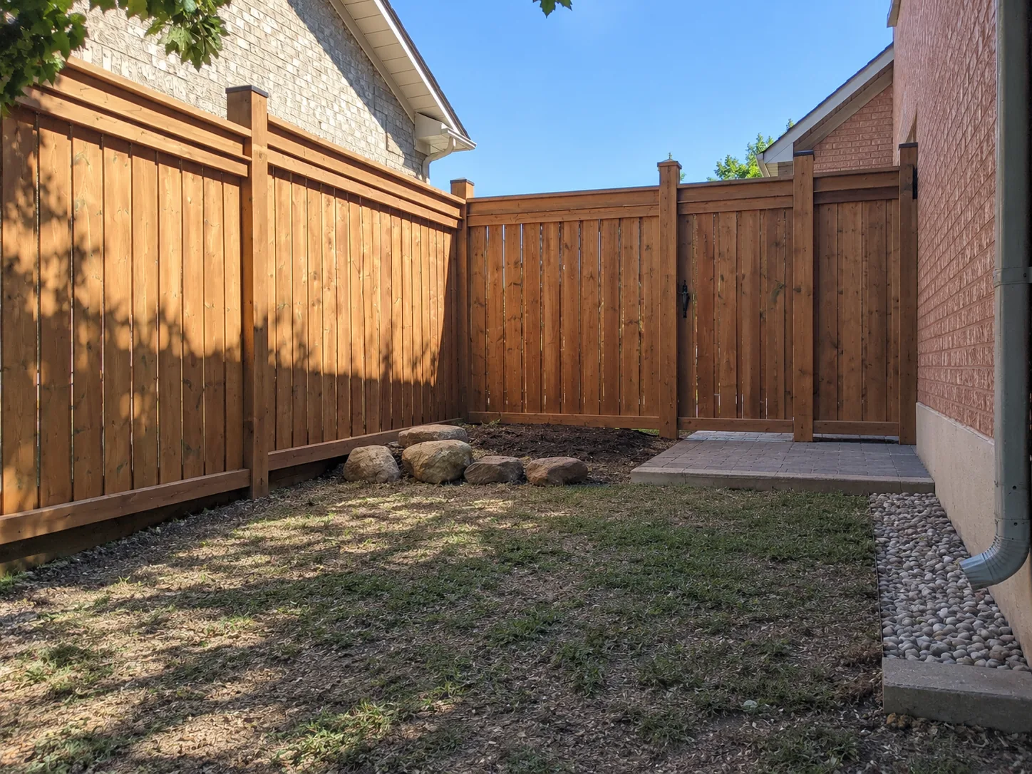 Pressure-treated wood fence with a matching gate and post caps beside a paver pad in a Toronto side yard